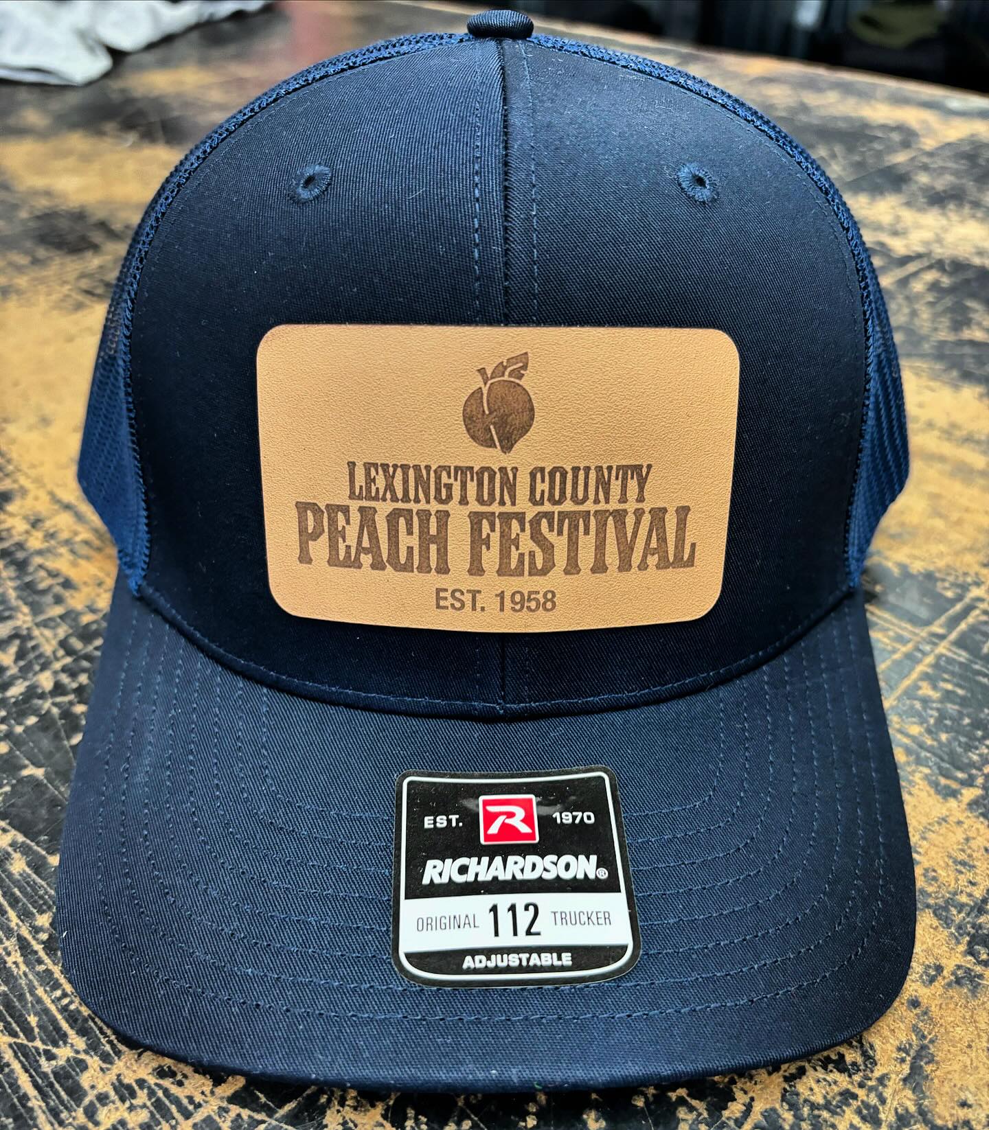 Navy blue Richardson 112 trucker hat with a leather patch featuring the Lexington County Peach Festival logo.