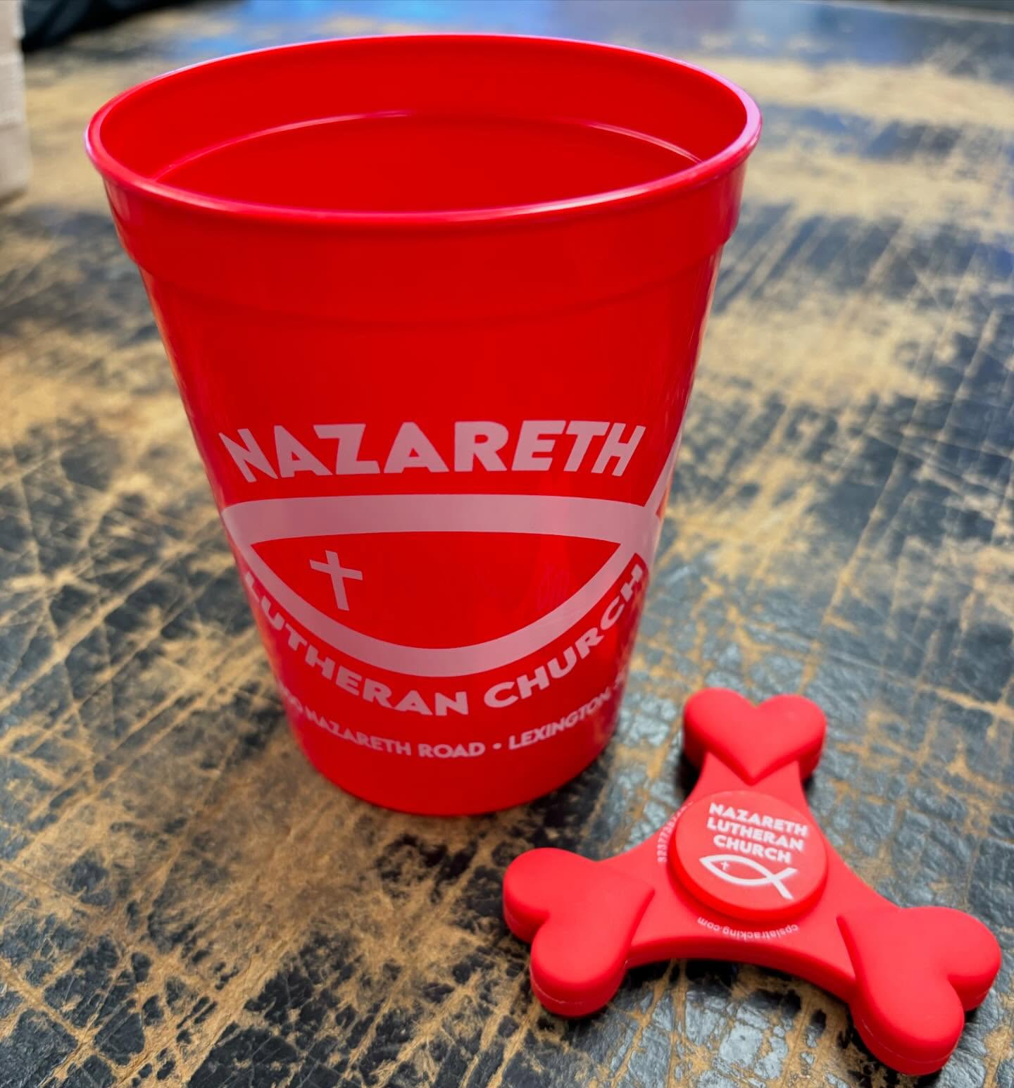 Red plastic cup and fidget spinner featuring the Nazareth Lutheran Church logo.