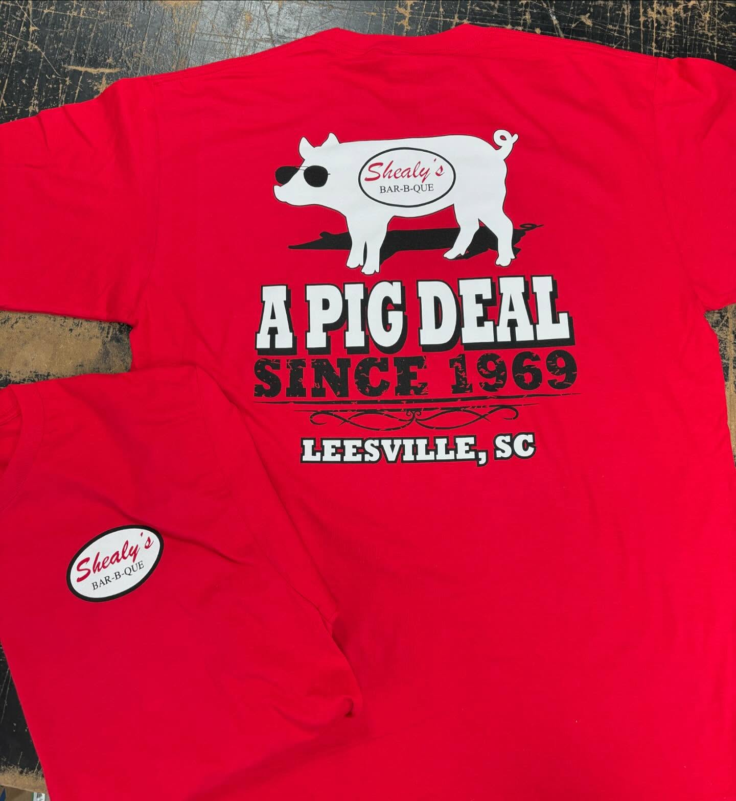 Red T-shirt with Shealy’s BBQ logo and “A Pig Deal Since 1969” slogan.